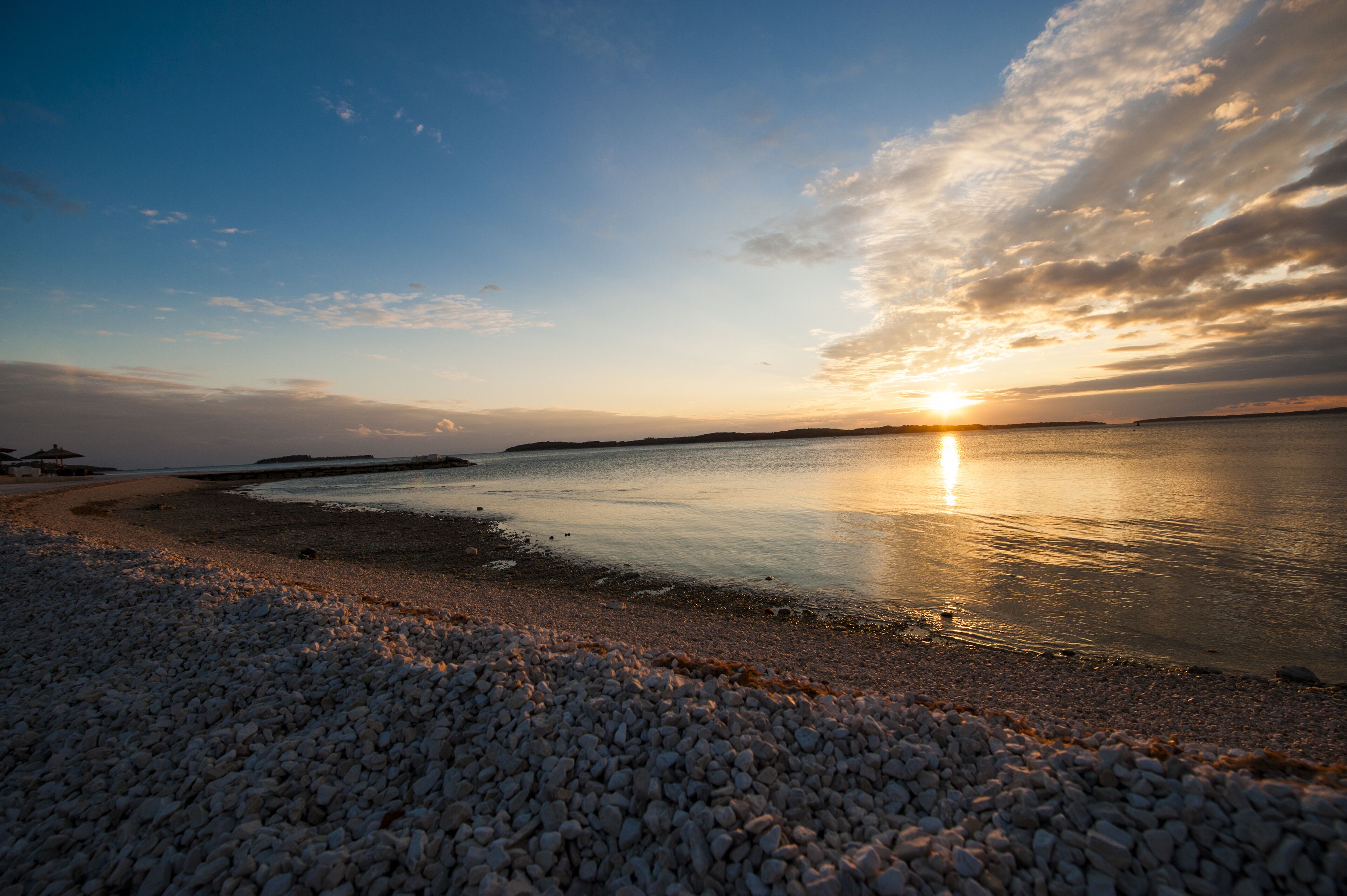 Une plage de galets avec un coucher de soleil sur l’eau.