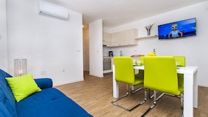 A modern living room with a blue sofa and bright green chairs, a kitchen with white cabinets, and a TV mounted on the wall. - Vacation apartment right by the sea-50 m from the beach (Fažana)