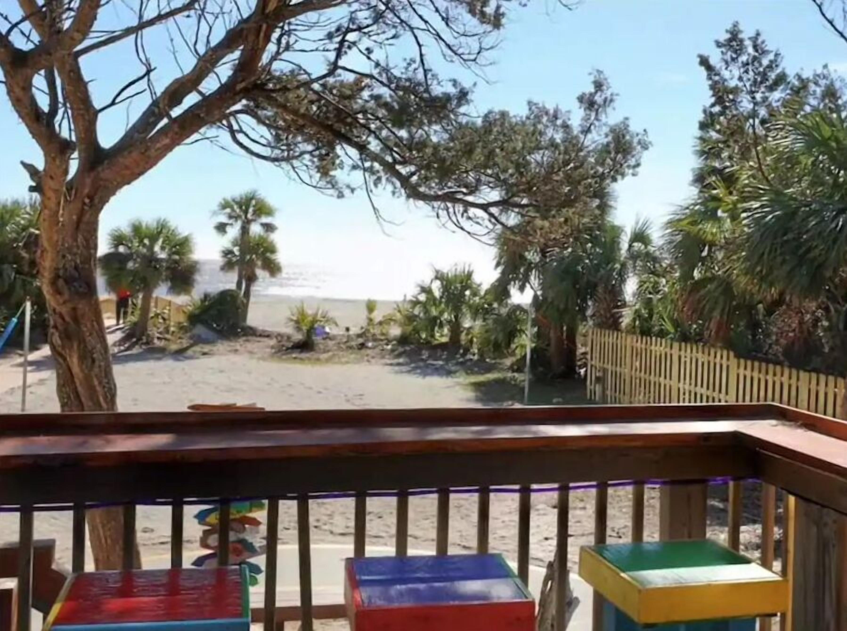 Une vue sur la plage depuis une terrasse en bois, agrémentée de blocs de couleurs vives et d’une clôture en bois.
