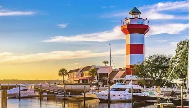 Un puerto deportivo con un faro destacado, barcos amarrados y una masa de agua tranquila que refleja el cielo.