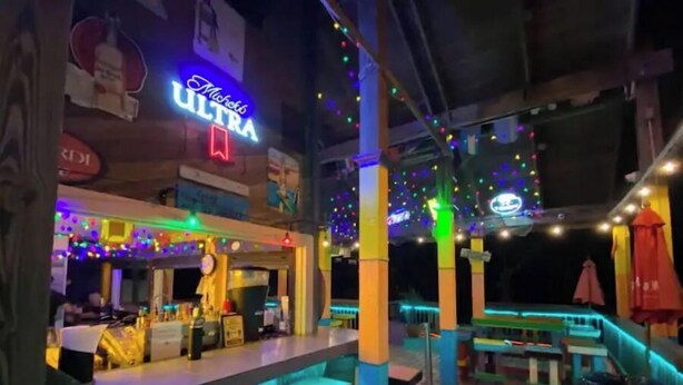 Uma área de bar com letreiro de neon, deck de madeira e luzes de Natal coloridas.