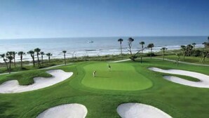 Um campo de golfe com bunkers de areia e vista para o oceano.