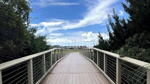 Uma ponte de madeira para pedestres com grades de metal, cercada por árvores e edifícios ao fundo.