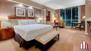 A hotel room with a large bed, a desk, a chair, a bench, and a view of the city at night. - MGM Signature-29-819 F1 Track & Strip View Studio (Las Vegas)