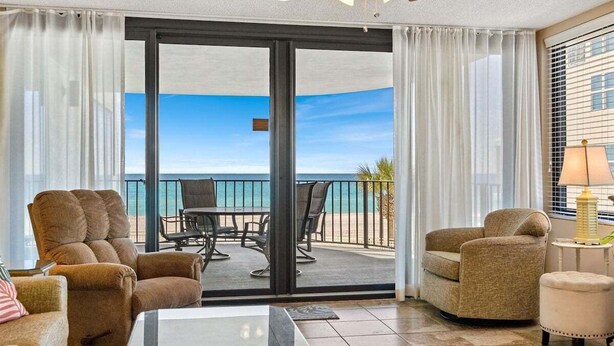 Habitación con vista al océano, puerta corrediza de vidrio, una mesa, dos sillas y una lámpara.