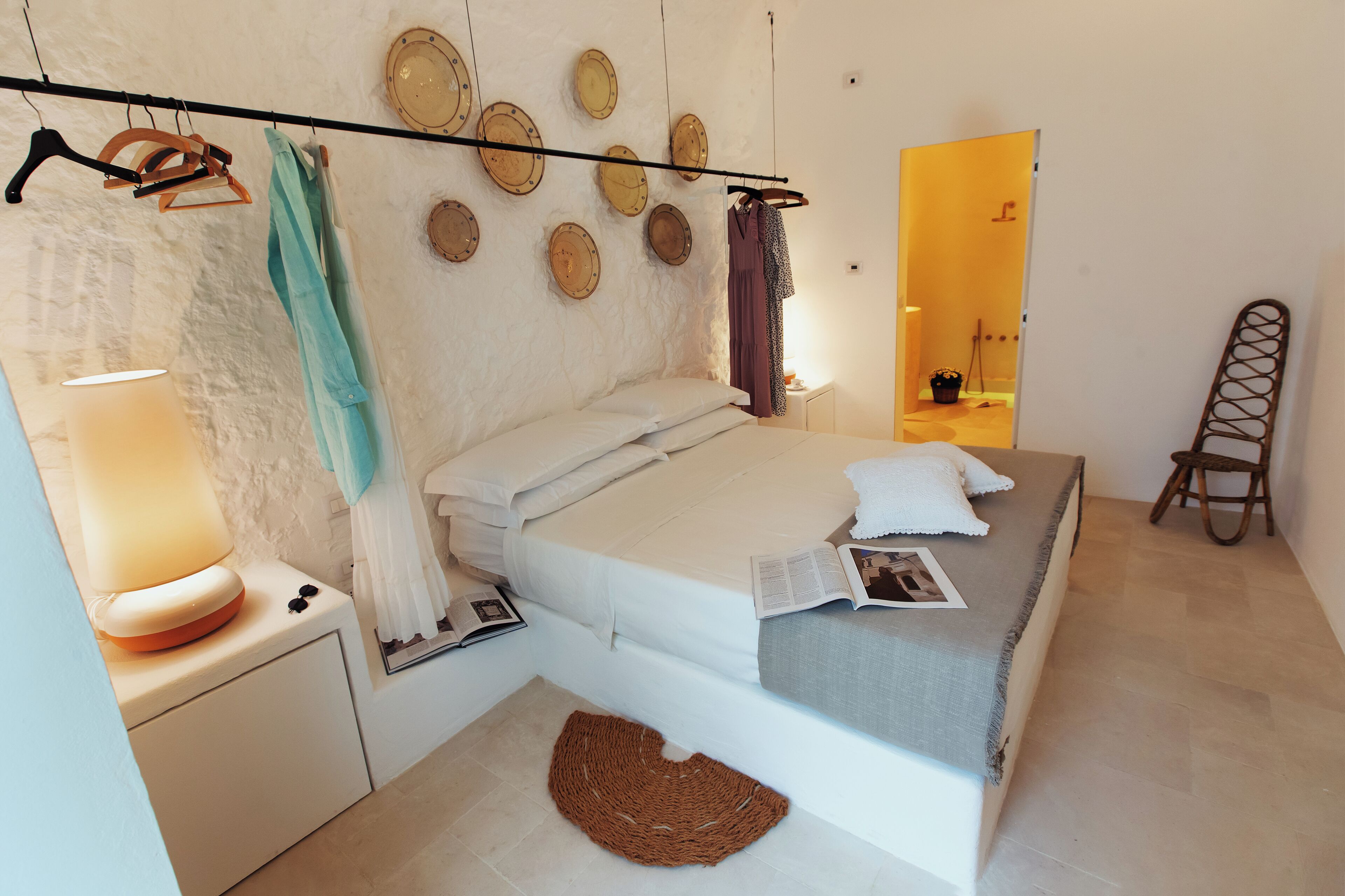 Una camera da letto con un letto, un comodino con una lampada, un appendiabiti con vestiti e uno specchio a parete.