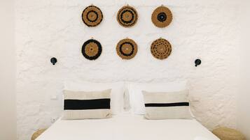 Una cama con dos almohadas, una pared blanca con textura y seis tapices tejidos.