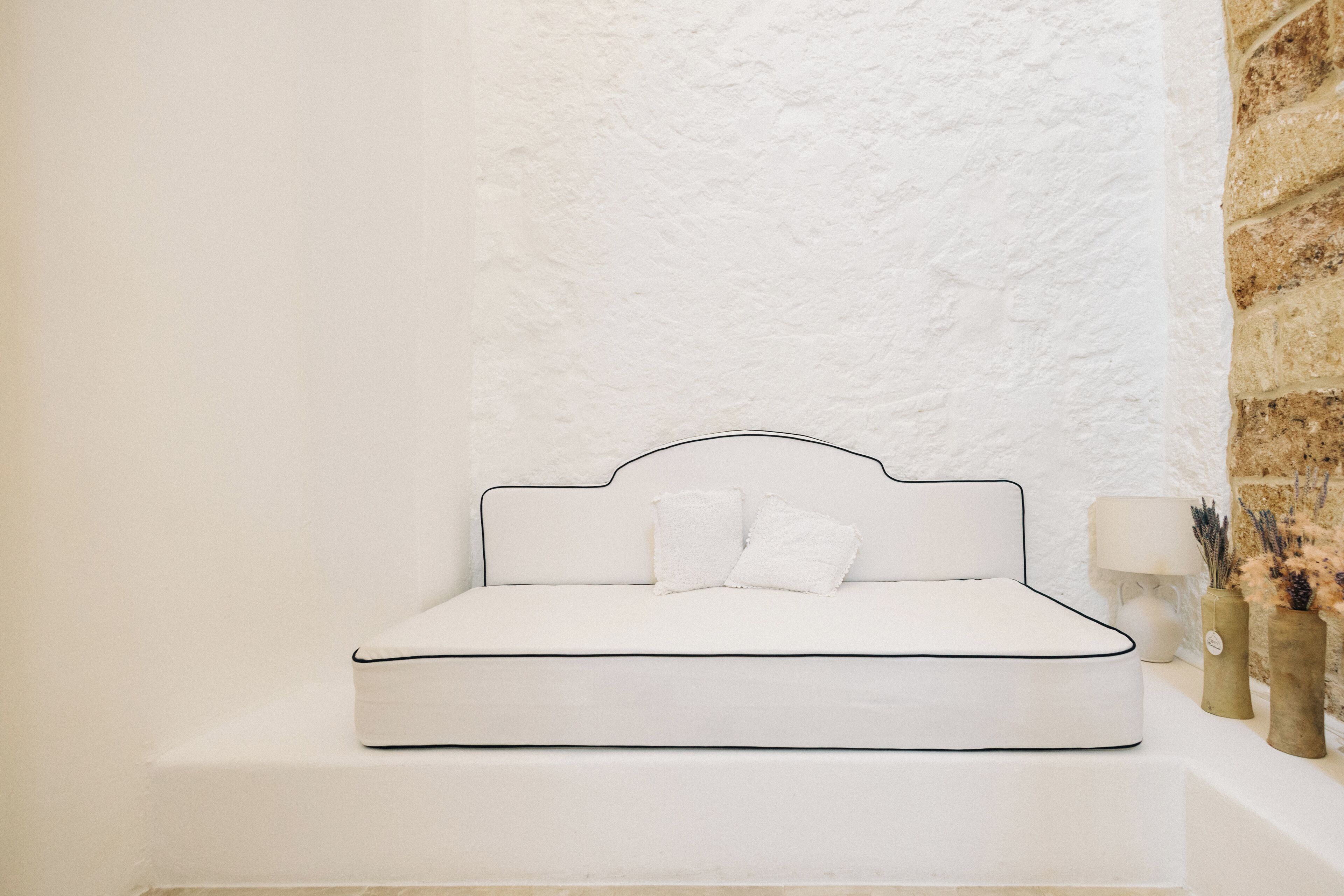 A white sofa with a black frame against a textured white wall, accompanied by a lamp and decorative vases.