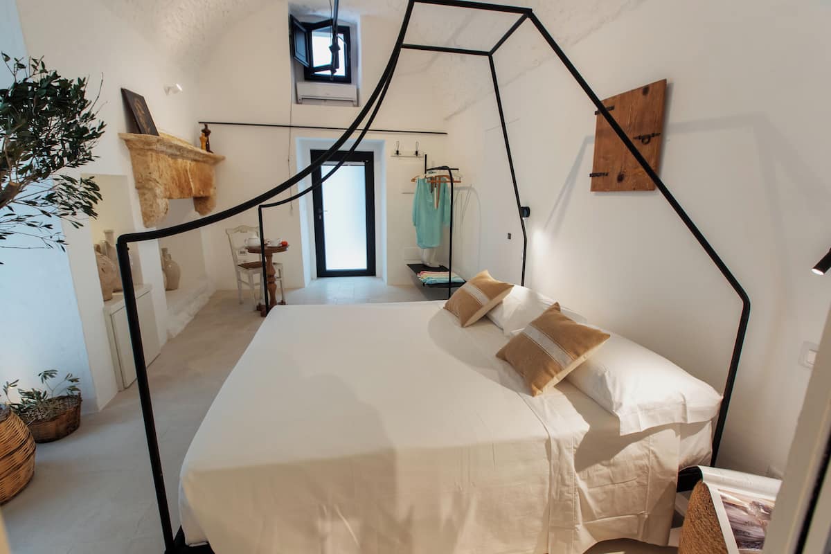 Quarto com cama, cadeira suspensa, mesinha, planta e janela.