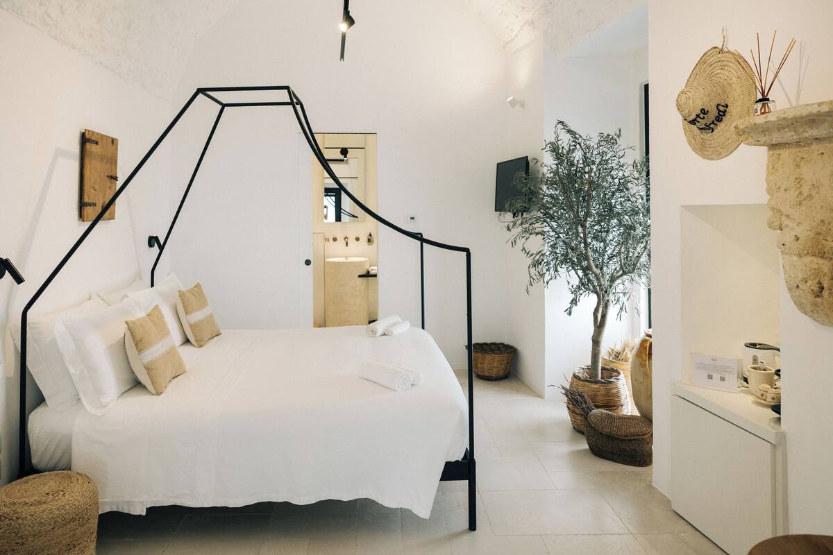 Quarto moderno com cama, cabeceira de madeira, TV na parede e uma planta em vaso.