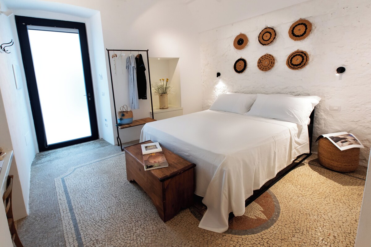 A bedroom with a bed, a bedside table with a magazine, a mirror, a wardrobe, and a wall with circular decorations.