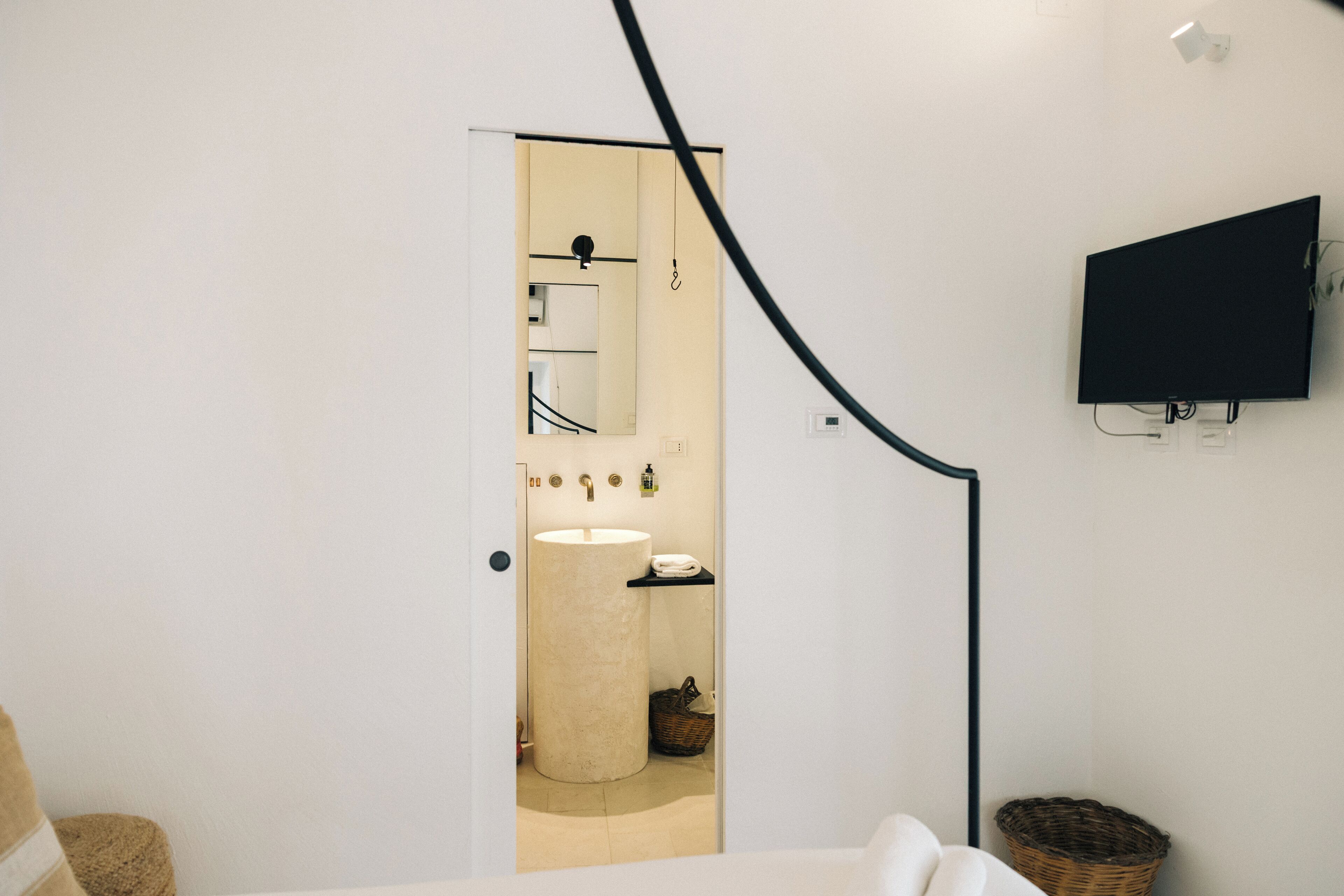 Ein modernes Badezimmer mit einem großen Waschbecken, einem Spiegel und einem schwarzen Fernseher an der Wand.