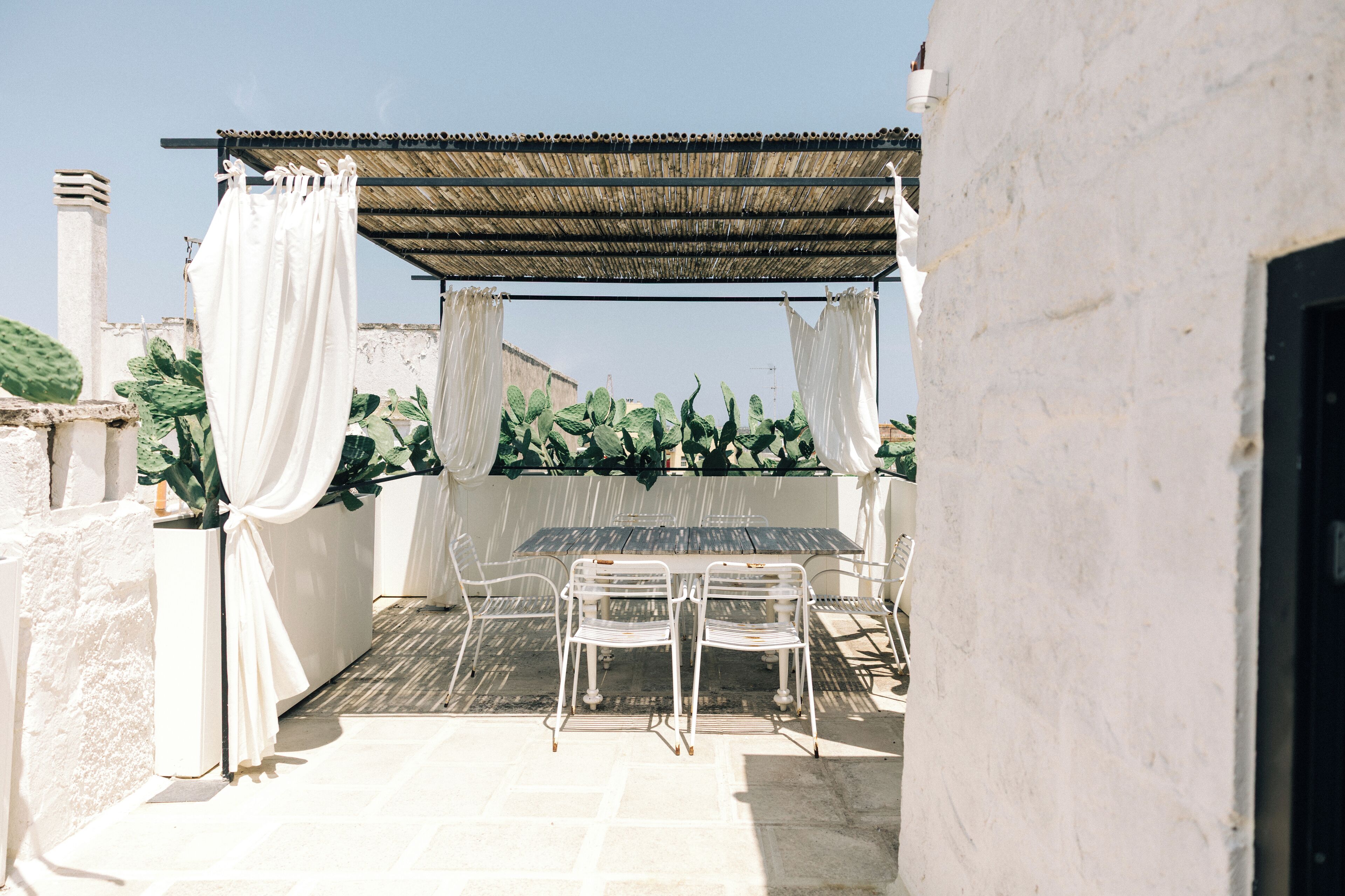 Une terrasse extérieure avec une table et des chaises, une pergola agrémentée de rideaux blancs et des plantes en pot.