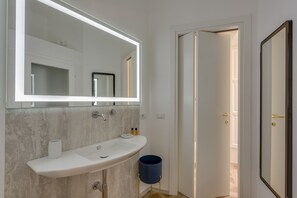 Een moderne badkamer met een witte wasbak, een grote spiegel en een blauwe prullenbak.