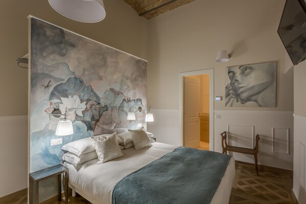 Een slaapkamer met een groot abstract schilderij aan de muur, een bed met witte beddengoed en een houten bankje.