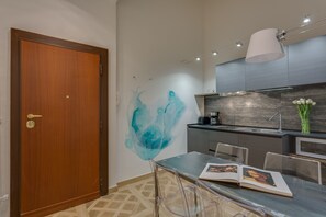Een moderne keuken met een houten deur, een transparante glazen tafel en abstracte wanddecoratie in blauw.