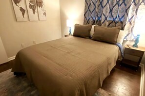 A neatly made bed with a beige bedspread, a nightstand with a lamp, and a world map on the wall.
