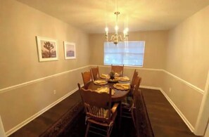 A dining room with a round table set for six, surrounded by wooden chairs.