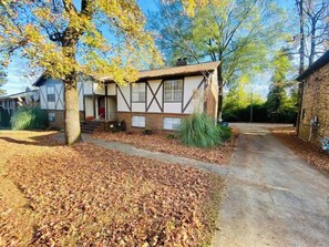 A two-story house with a front porch, a chimney, and a driveway leading to a garage.