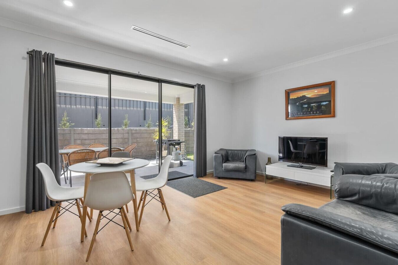 A modern living room with a dining area, a fireplace, and a large window overlooking a garden.
