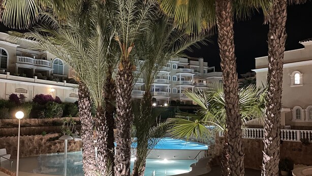 Ein Nachtblick auf ein Resort mit Swimmingpool, Palmen und einer gut beleuchteten Gebäudefassade.