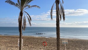 Ein Strand mit Palmen, einem Rettungsschwimmer-Schild und einer entfernten Personengruppe.