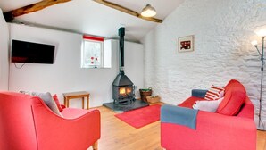 Un salon chaleureux avec une cheminée, des canapés rouges, une table en bois et un mur en pierre.