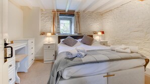 Une chambre avec un mur en pierre, un lit avec des oreillers et une couverture, deux tables de chevet avec des lampes et une fenêtre avec des rideaux.