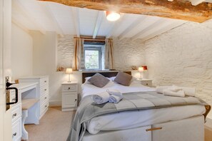 Une chambre avec un mur en pierre, un lit avec des oreillers et une couverture, deux tables de chevet avec des lampes et une fenêtre avec des rideaux.