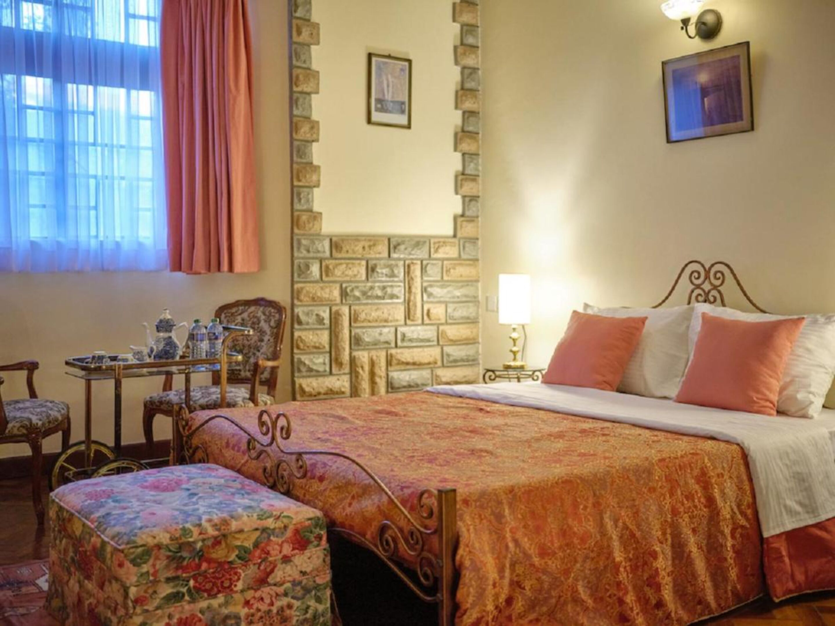 Un dormitorio con cama, una mesa con tetera, sillas y una pared de piedra.