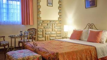 Un dormitorio con cama, una mesa con tetera, sillas y una pared de piedra.