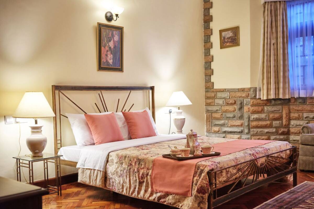 A neatly arranged bedroom with a bed, bedside lamps, a small table, and a decorative tray.