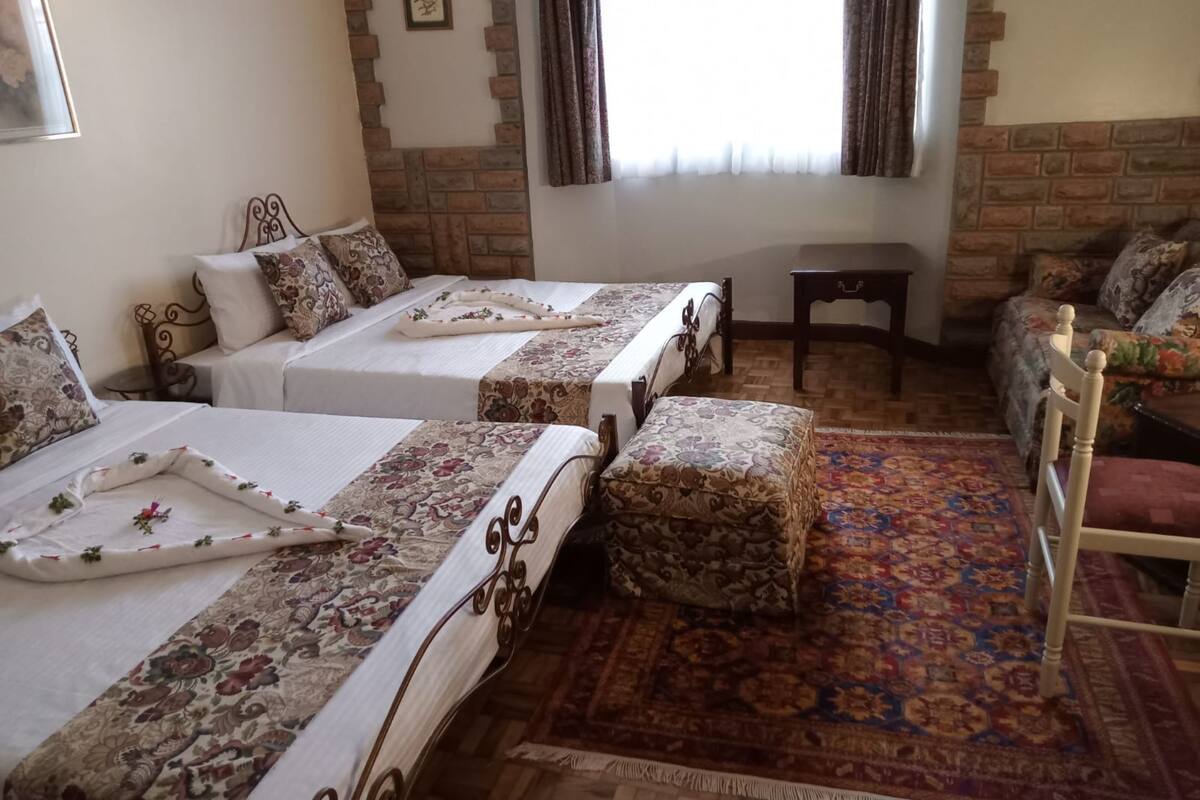 A hotel room with two beds, a small table, a chair, and a patterned rug.