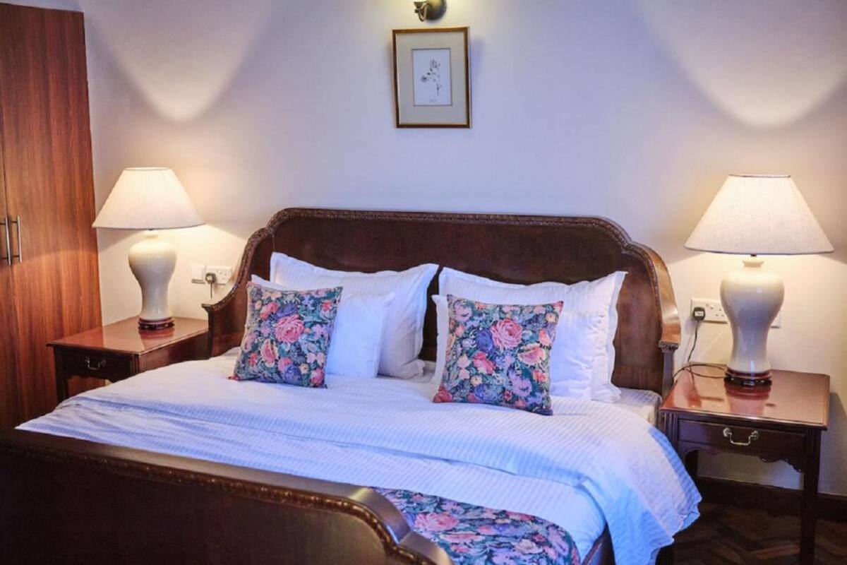 A neatly made bed with floral pillows, two bedside lamps, and a framed picture on the wall.
