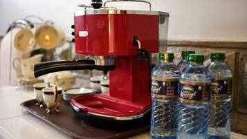 Une machine à café rouge, posée sur un plateau avec quatre bouteilles d’eau et quelques tasses.