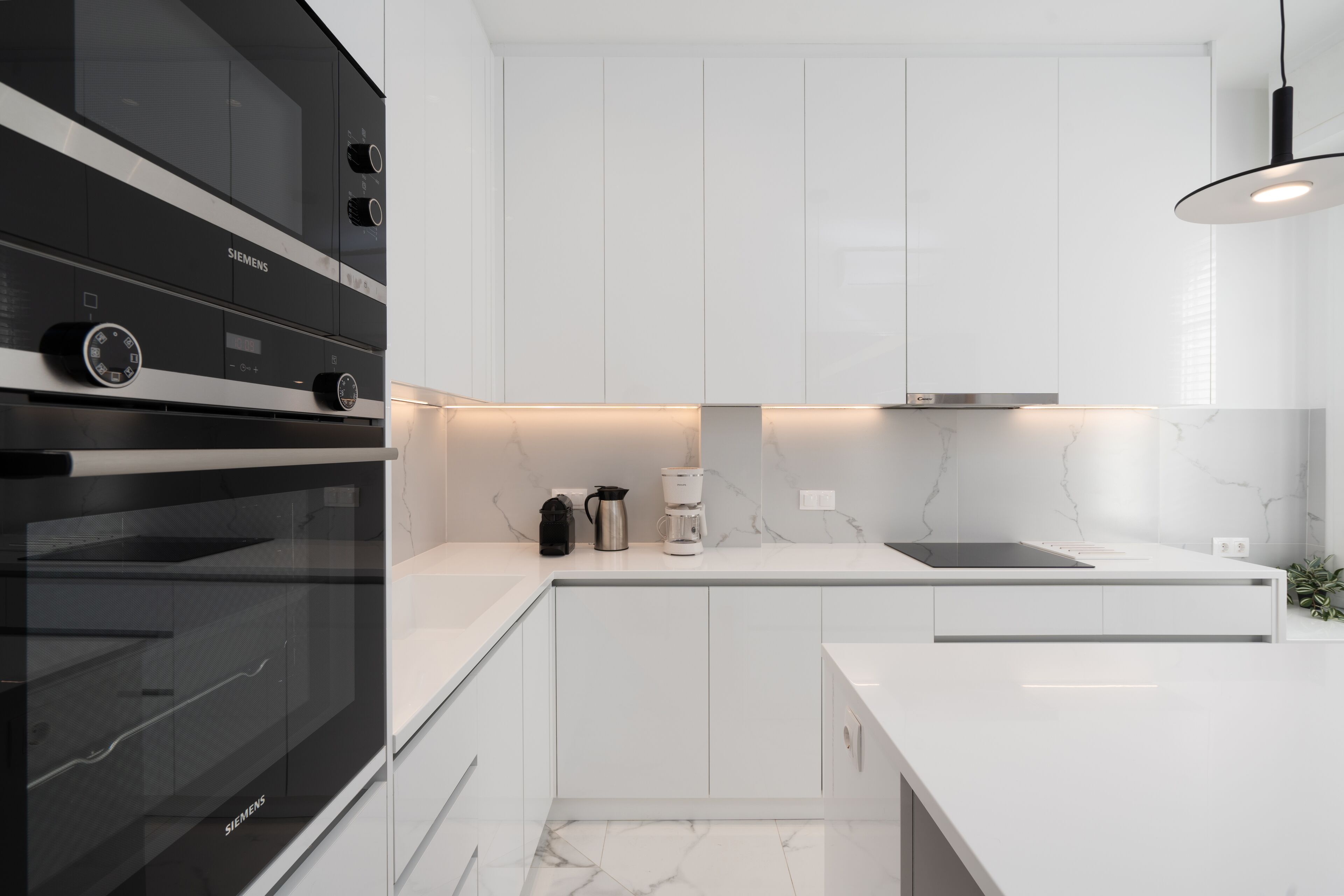 A modern kitchen with white cabinetry, a black oven, and a marble backsplash.