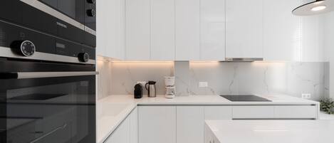 A modern kitchen with white cabinetry, a black oven, and a marble backsplash.