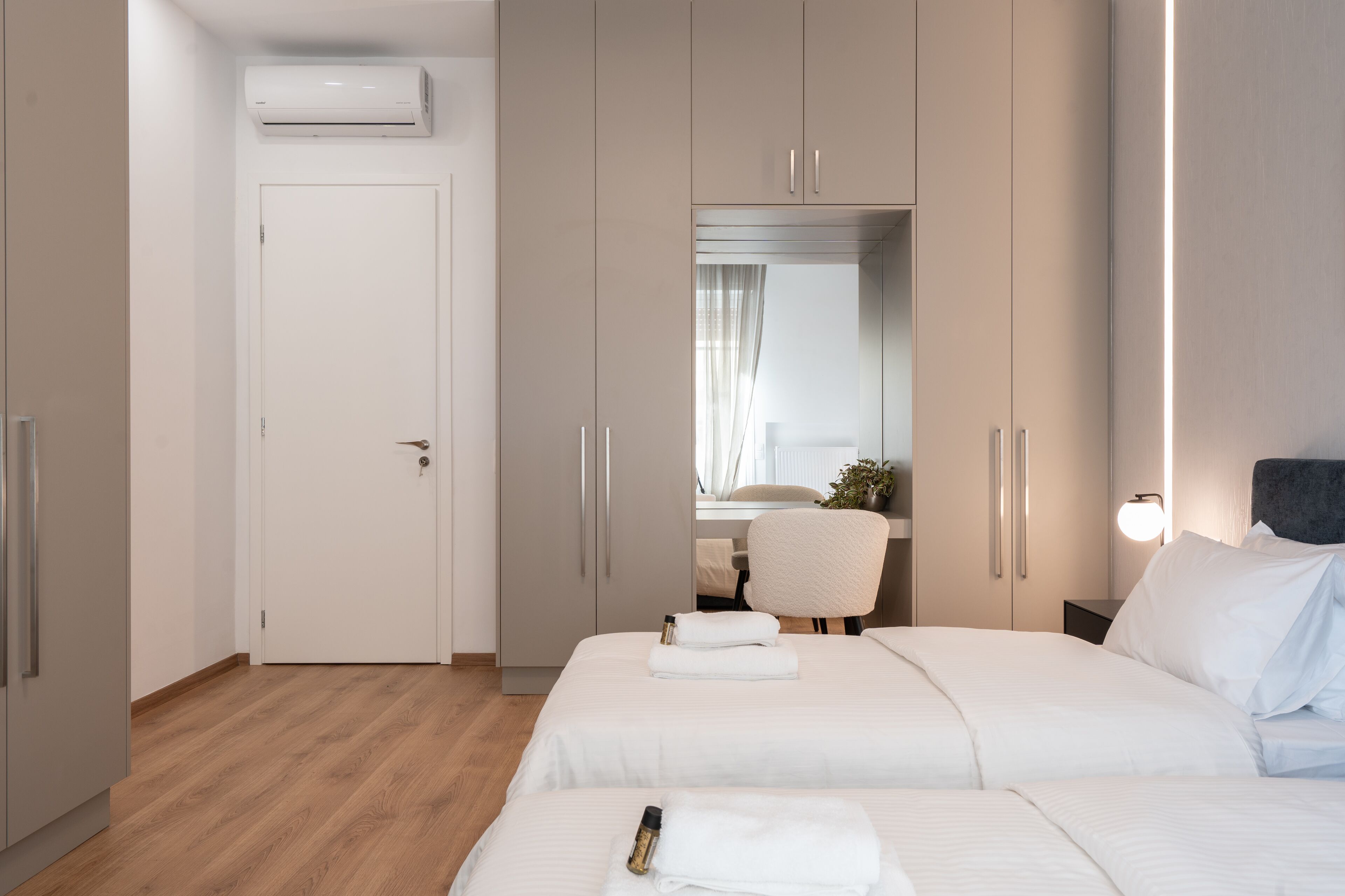 A modern hotel room with two beds, a desk, and a wardrobe.