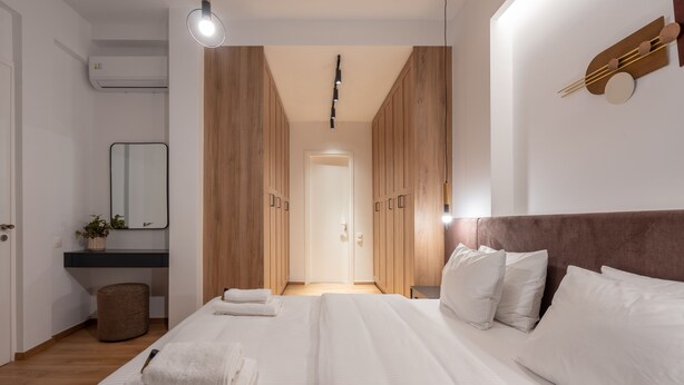 A modern bedroom with a large bed, wooden wardrobe, a bedside table, and a mirror.