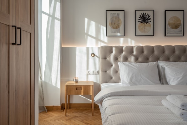 Une chambre à coucher avec une tête de lit capitonnée, une table de chevet avec une lampe et des œuvres d’art accrochées au mur.