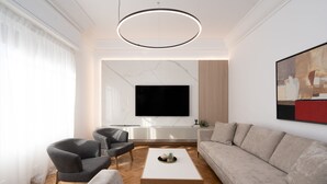 A modern living room with a flat-screen TV, grey sofas, a coffee table, and a wooden floor.