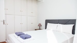 A neatly made bed with white and blue towels, a grey headboard, and a small bedside table with a lamp. - Gorgeous apt in Faliro with view (Palaio Faliro)