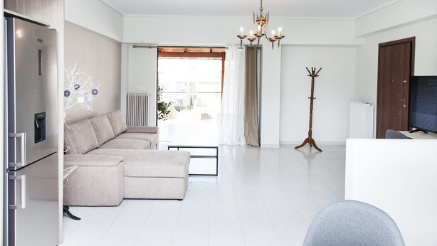 A modern living room with a sectional sofa, a dining table, a coat rack, and a television. - Gorgeous apt in Faliro with view (Palaio Faliro)