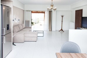 A modern living room with a sectional sofa, a dining table, a coat rack, and a television.
