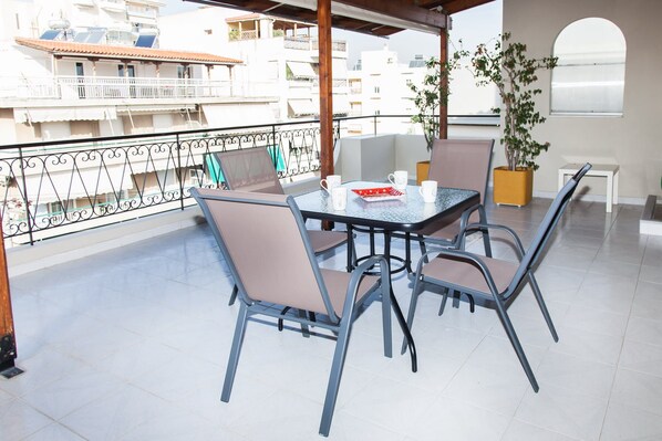 A balcony with a table and chairs, a potted plant, and a view of buildings in the background. - Gorgeous apt in Faliro with view (Palaio Faliro)