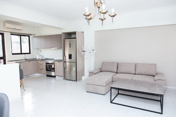 A modern kitchen with stainless steel appliances, a built-in oven, and a refrigerator. There is a beige sectional sofa and a coffee table in the living area.