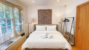 Un letto ben rifatto con asciugamani arrotolati, una testiera in legno, un pannello decorativo, una lampada da terra e un'armadio.