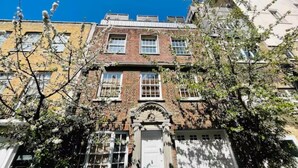 Un edificio a più piani con facciata in mattoni, ampie finestre e un ingresso centrale caratterizzato da un arco decorativo.