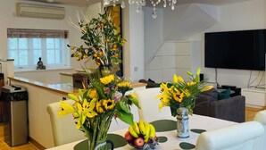 Un'area pranzo moderna con un lampadario, un tavolo da pranzo con sedie, un vaso con fiori e una ciotola di frutta.