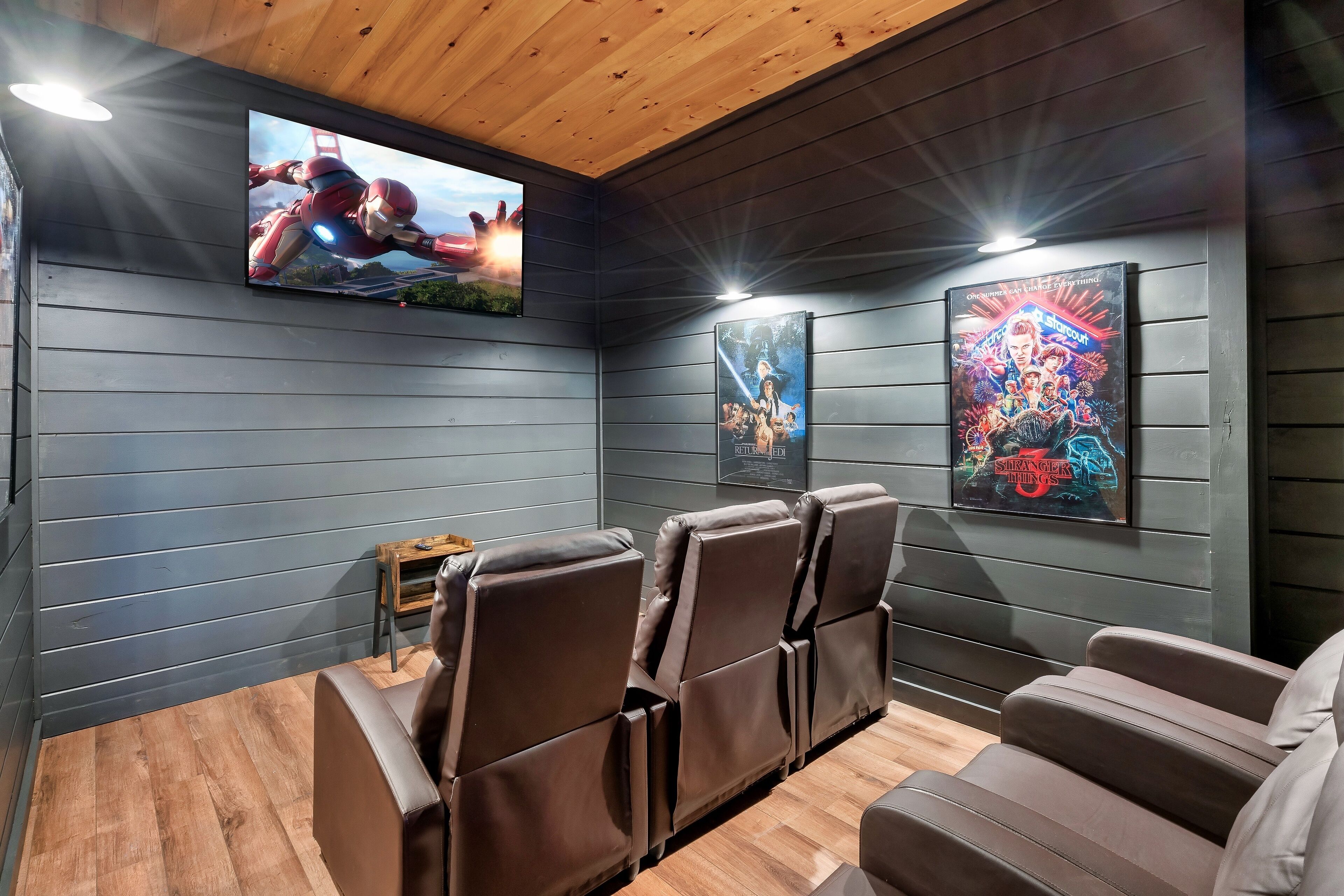 A home theater room with dark wooden walls, a wooden ceiling, and a large flat-screen TV mounted on the wall.